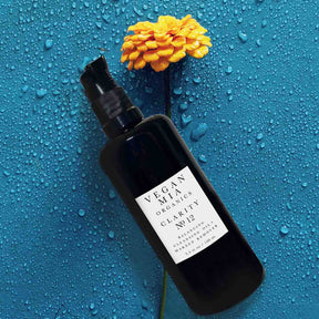 Vegan Mia Organics Clarity Balancing Cleansing Oil and Makeup Remover Bottle on Blue Background with Yellow Flower